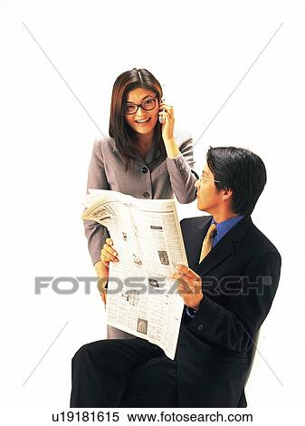 Stock Photography - Man holding newspaper and looking at woman smiling and using mobile phone, portrait for woman. Fotosearch