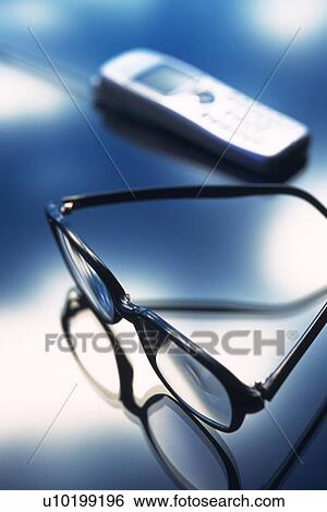 Stock Photograph - Mobile phone and glasses, high angle view, soft focus. Fotosearch