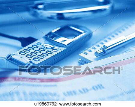 Stock Image - Mobile phone and newspaper put on desk with stationery, high angle view, close up, toned image. Fotosearch