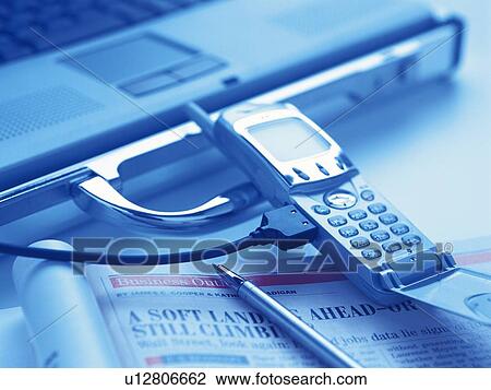 Stock Image - Mobile phone being connected to laptop, high angle view, toned image. Fotosearch