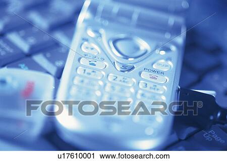 Stock Image - Mobile phone being connected to laptop, high angle view, close up, toned image. Fotosearch