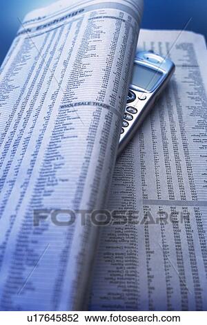 Stock Image - Mobile phone put between folded newspaper, high angle view, close up. Fotosearch