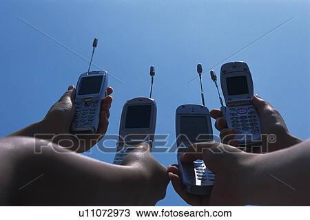 Stock Image - Four People Holding a Mobile Phone, Low Angle View. Fotosearch
