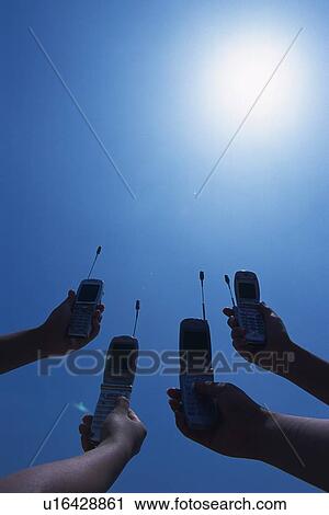 Stock Image - Four People Holding a Mobile Phone, Low Angle View. Fotosearch