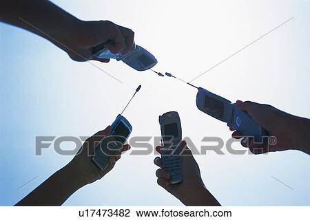 Stock Image - Four People Holding a Mobile Phone, Low Angle View. Fotosearch