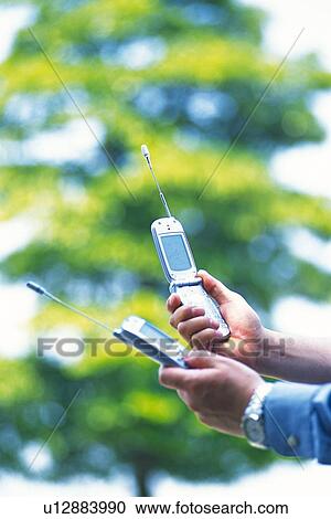 Stock Image - Two People Holding a Mobile Phone, Side View. Fotosearch