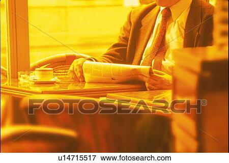 Stock Photo - Businessman sitting and holding newspaper at table in cafe, toned image. Fotosearch