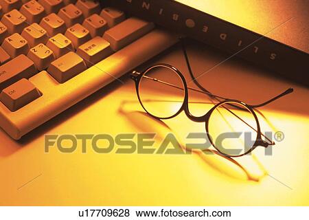 Stock Photo - Glasses and computer keyboard on desk, high angle view. Fotosearch