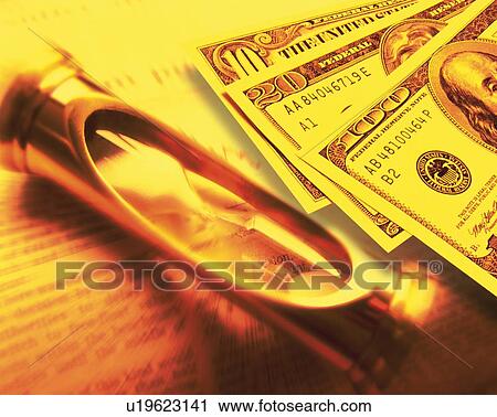 Stock Image - Hourglass and US banknotes on newspaper, blurred motion, toned image, high angle view. Fotosearch