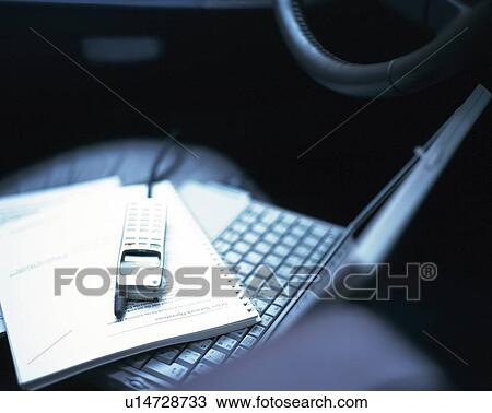Stock Image - Notebook and mobile phone on laptop in the car, high angle view. Fotosearch
