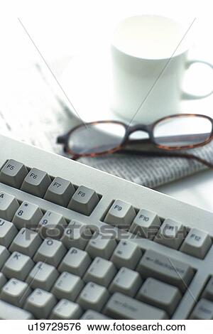 Stock Photograph - Keyboard, Coffee Cup, Newspaper and Glasses on the Desk, High Angle View. Fotosearch