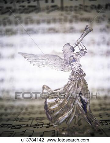 Stock Image - Glass angel playing trumpet and image of sheet music, rear view. Fotosearch