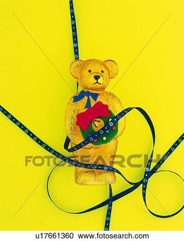 Ribbons around teddy bear holding Christmas wreath, yellow background View Large Photo Image Stock Image - Ribbons around teddy bear holding Christmas wreath, yellow background. Fotosearch