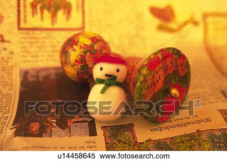 Stock Photography - Snowman leaning on Christmas ornament on newspaper, front view. Fotosearch