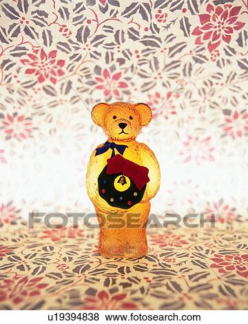 Stock Photo - Teddy bear standing and holding Christmas wreath, front view, composition. Fotosearch