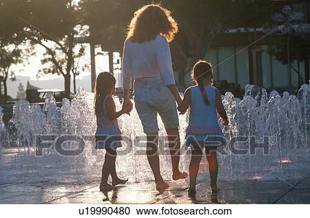 Stock Image - A mother and her twin daughters playing in the water fountains. Fotosearch