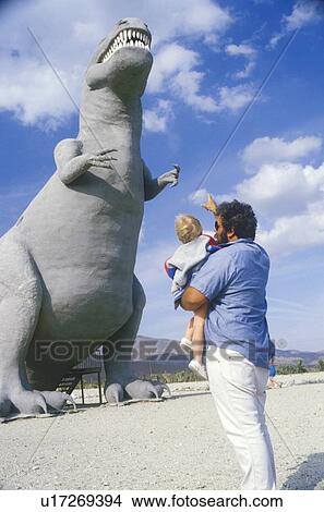 Picture - Parent and baby looking at a statue of a dinosaur. Fotosearch