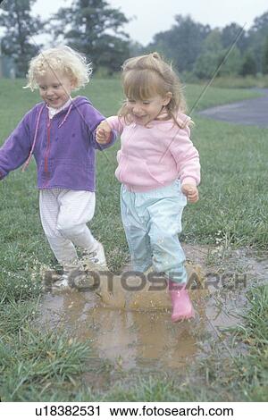 Stock Image - Two children jumping over a puddle. Fotosearch
