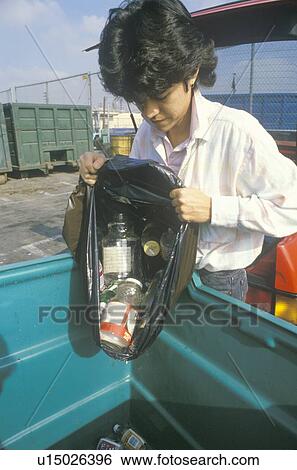 Stock Photograph - A boy emptying recyclables into a blue bin at a recycling center. Fotosearch