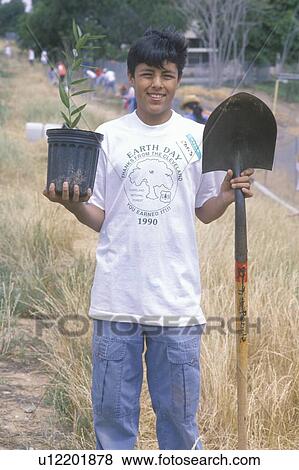 Stock Photo - A teenage boy holding a plant and a shovel during Earth Day participation. Fotosearch
