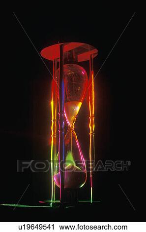 Stock Image - An hourglass illuminated by multi-colored laser lights shining through. Fotosearch