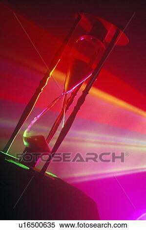 Stock Photography - An hourglass illuminated by multi-colored laser lights shining through. Fotosearch
