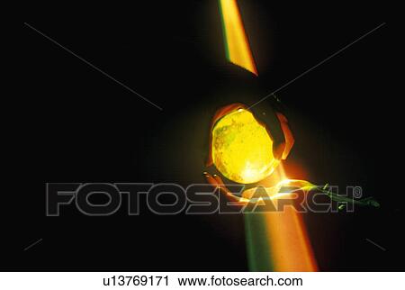 Stock Image - Hands holding a glowing crystal sphere as orange laser light shines down. Fotosearch
