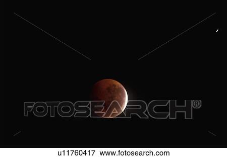 Stock Photo - A full moon mostly covered by Earth's shadow during a lunar eclipse against a black starless sky. Fotosearch