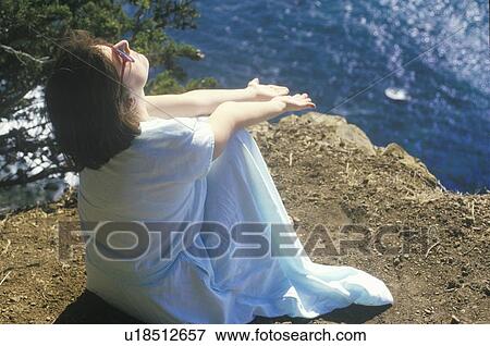 Stock Photo - A woman meditating on the coastline. Fotosearch