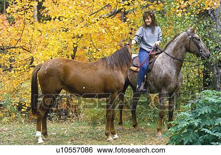 Stock Photograph - Woman on horseback leading horse. Fotosearch