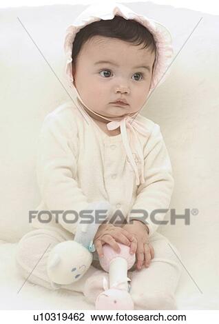 Stock Image - Close-up of a baby girl sitting on a bed. Fotosearch