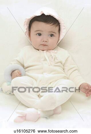 Stock Photograph - Close-up of a baby girl sitting on a bed. Fotosearch