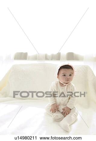 Stock Image - High angle view of a baby girl sitting on a bed. Fotosearch
