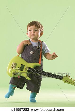 Stock Image - Portrait of a baby boy holding a guitar. Fotosearch