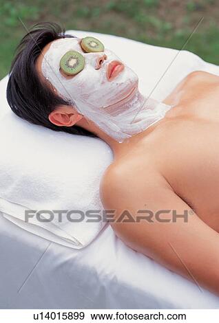 Stock Photo - Man getting a facial with kiwis on his eyes . Fotosearch