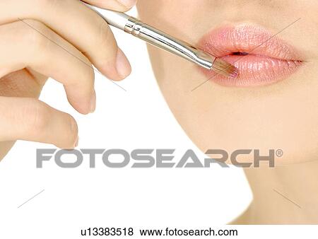 Stock Photo - Close-up of a woman applying lipstick with a lip brush. Fotosearch