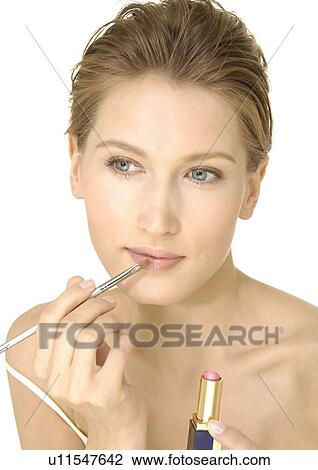 Stock Image - Close-up of a young woman applying lipstick with a lip brush. Fotosearch