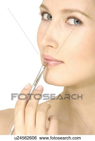 Portrait of a young woman applying lipstick with a lip brush View Large Photo Image Stock Photograph - Portrait of a young woman applying lipstick with a lip brush. Fotosearch