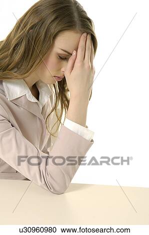 Stock Image - Businesswoman sitting at a table with her head in her hand. Fotosearch