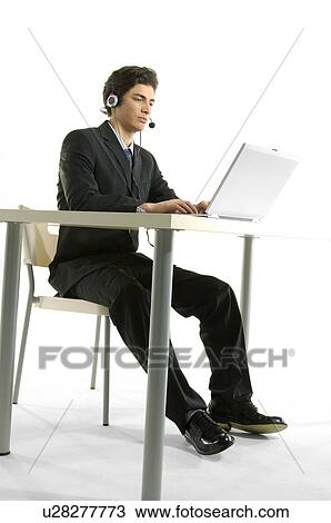 Male customer service representative sitting at a table and using a laptop View Large Photo Image Stock Image - Male customer service representative sitting at a table and using a laptop. Fotosearch