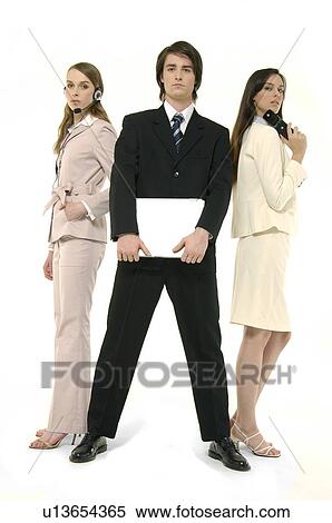 Stock Photography - Portrait of a businessman holding a laptop with two businesswomen standing behind him. Fotosearch
