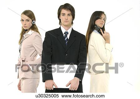 Stock Photography - Portrait of a businessman holding a laptop with two businesswomen standing behind him. Fotosearch