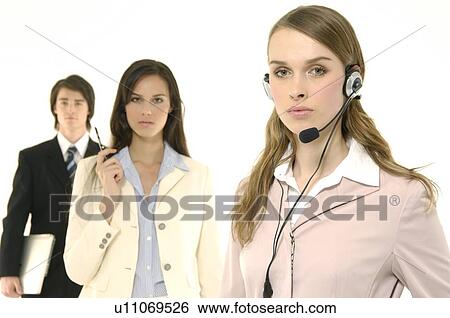Stock Photograph - Portrait of a female customer service representative talking on a headset with her colleagues standing behind her. Fotosearch