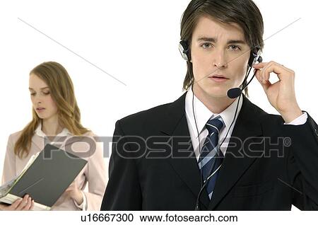 Stock Image - Portrait of a male customer service representative talking on a headset with a businesswoman standing behind him. Fotosearch