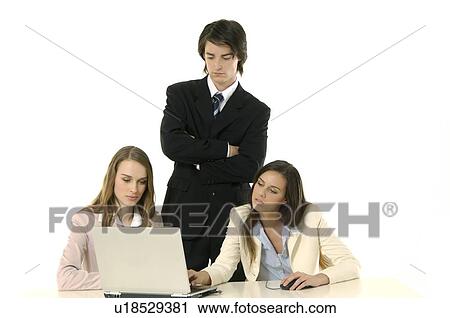 Stock Image - Two businesswomen working on a laptop with a businessman standing beside them. Fotosearch