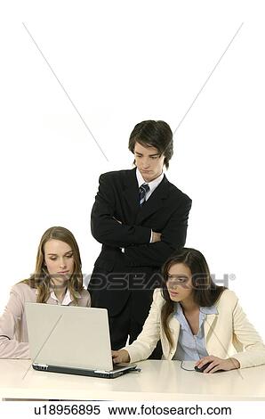 Two businesswomen working on a laptop with a businessman standing beside them View Large Photo Image Stock Photography - Two businesswomen working on a laptop with a businessman standing beside them. Fotosearch