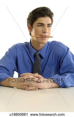 Stock Image - Businessman sitting at a desk and holding a pencil in his mouth. Fotosearch