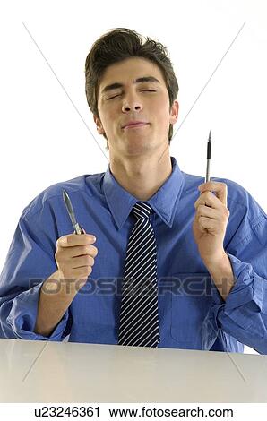 Stock Image - Businessman sitting at a desk and holding two pens. Fotosearch