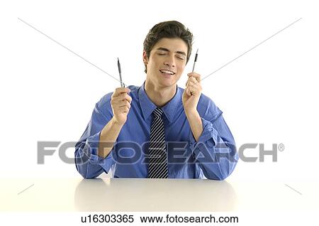 Businessman sitting at a desk and holding two pens View Large Photo Image Stock Photography - Businessman sitting at a desk and holding two pens. Fotosearch