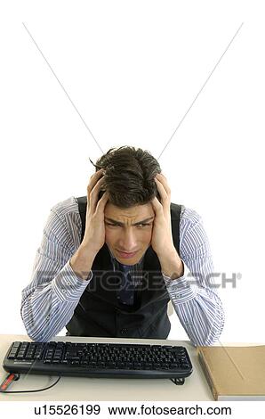 Stock Photo - Businessman sitting at a desk with his head in his hands in an office. Fotosearch